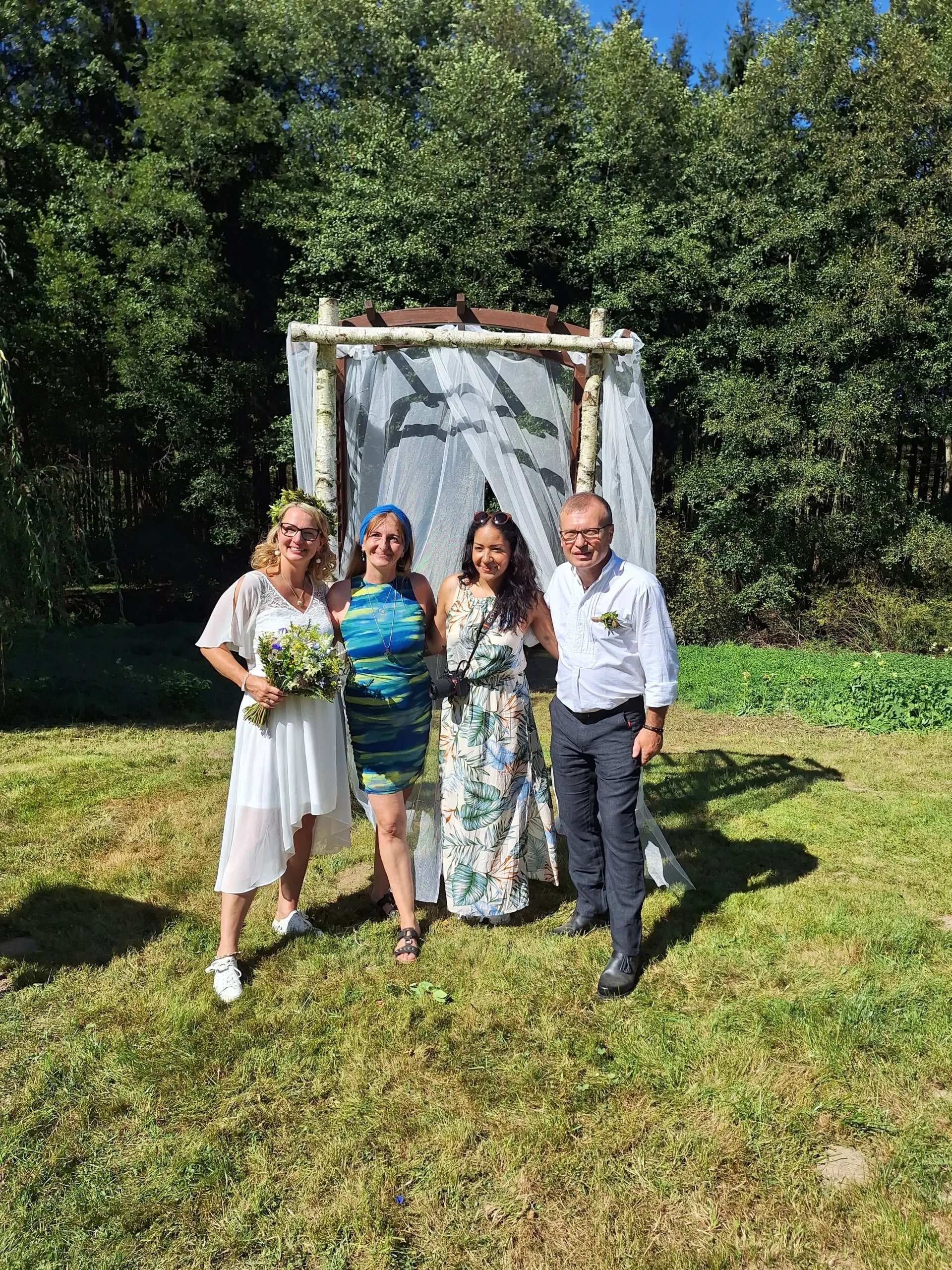 Hochzeitspaar mit Traurednerin und Fotografin vor dem Traubogen auf einer Wiese